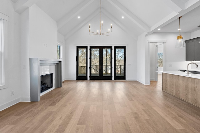 unfurnished living room with a wealth of natural light, french doors, a notable chandelier, and light wood-style flooring