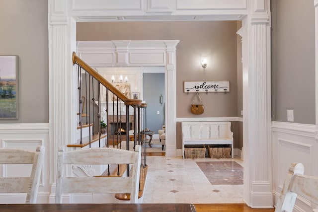 interior space with a wainscoted wall, a lit fireplace, a decorative wall, and an inviting chandelier