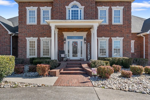 entrance to property with a shingled roof and brick siding