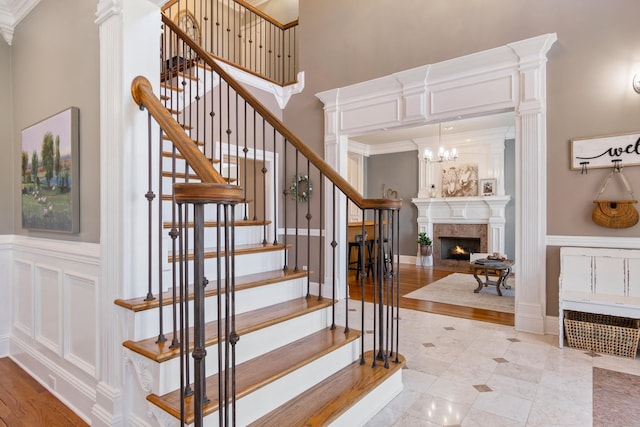 staircase with crown molding, a decorative wall, a high ceiling, wainscoting, and a lit fireplace