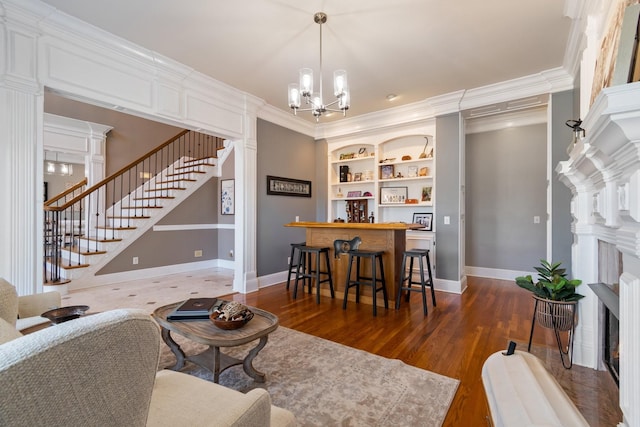 living area featuring decorative columns, ornamental molding, wood finished floors, stairs, and built in shelves