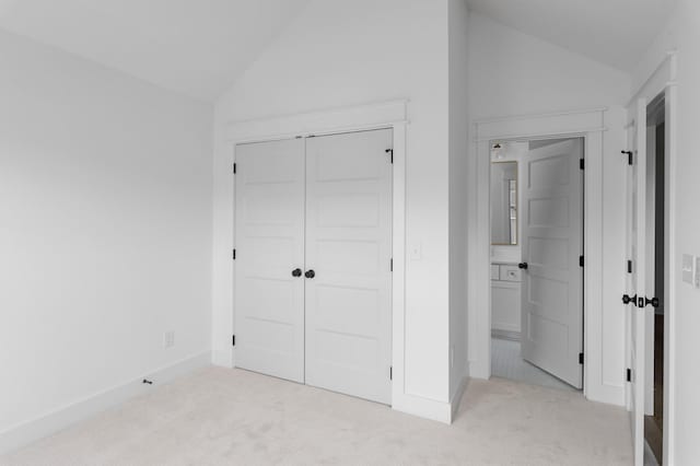 unfurnished bedroom with lofted ceiling, a closet, light carpet, and baseboards