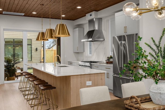 kitchen featuring wooden ceiling, high end refrigerator, a sink, wall chimney range hood, and a center island with sink