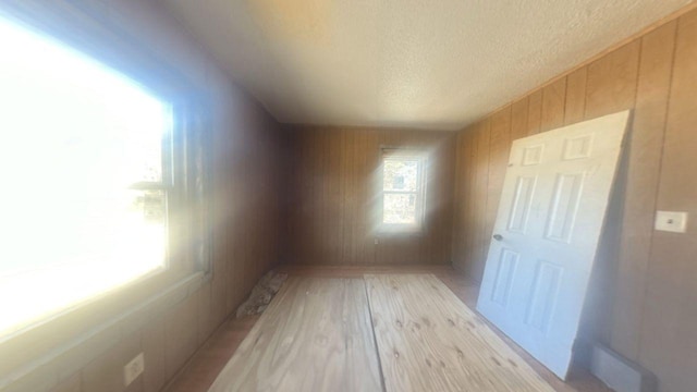 interior space featuring a textured ceiling, light wood finished floors, and wooden walls