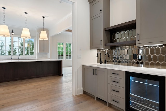 bar with light wood finished floors, beverage cooler, ornamental molding, decorative light fixtures, and backsplash