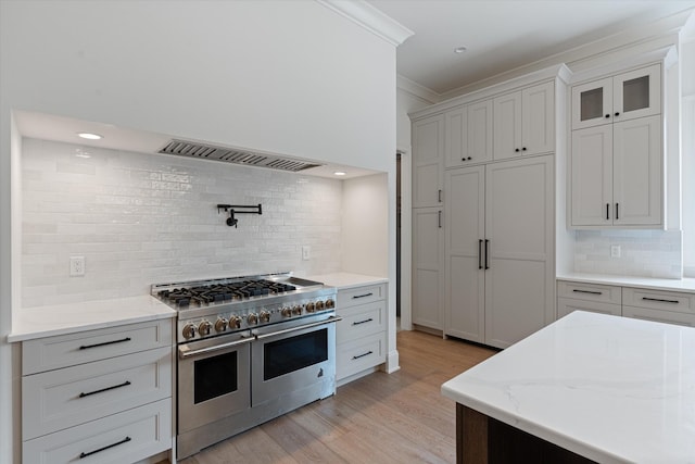 kitchen featuring range with two ovens, light stone counters, light wood-style floors, wall chimney range hood, and crown molding