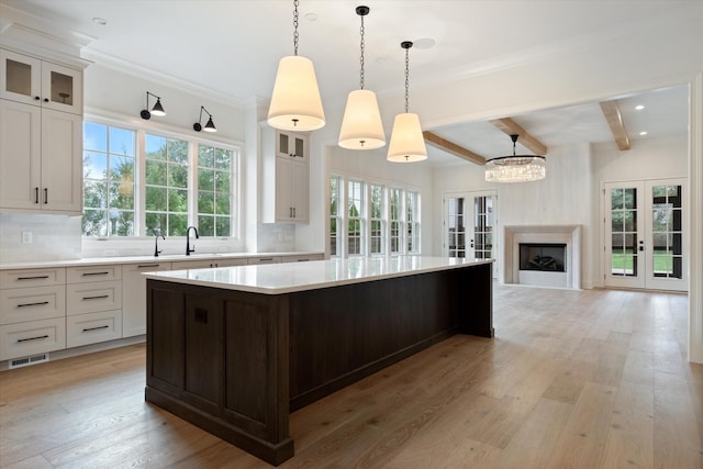 kitchen featuring light wood-style flooring, a kitchen island, light countertops, french doors, and backsplash