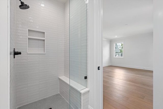 bathroom featuring a tile shower, baseboards, and wood finished floors