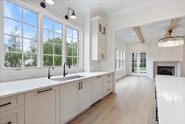 kitchen featuring tasteful backsplash, light countertops, light wood-style floors, a sink, and beamed ceiling