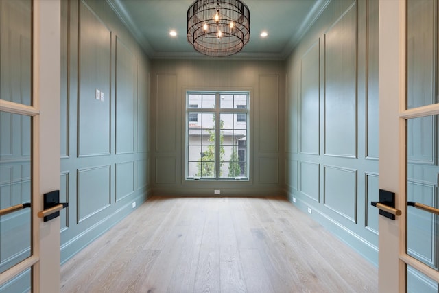 unfurnished room with crown molding, light wood finished floors, an inviting chandelier, and a decorative wall