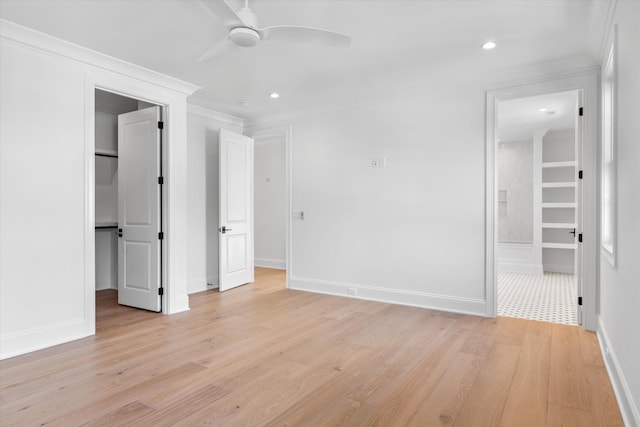 unfurnished bedroom with a walk in closet, crown molding, a closet, light wood-style flooring, and baseboards