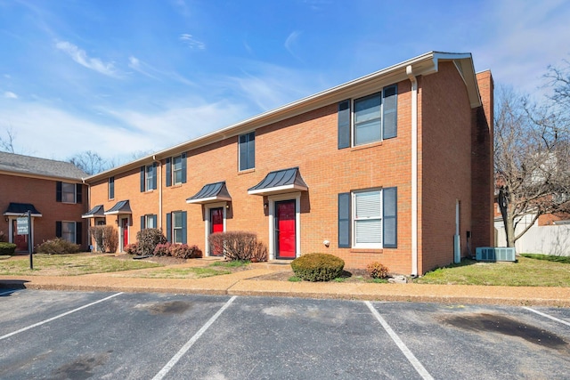 townhome / multi-family property with uncovered parking, cooling unit, and brick siding