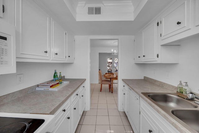 kitchen featuring crown molding, a tray ceiling, white cabinets, and a sink