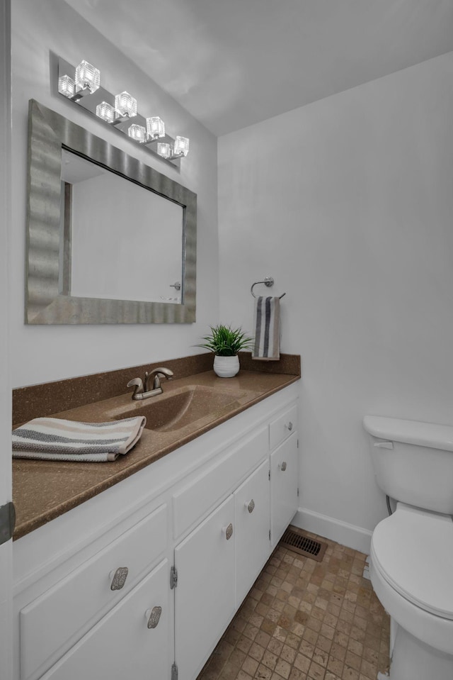 bathroom with toilet, vanity, visible vents, and baseboards