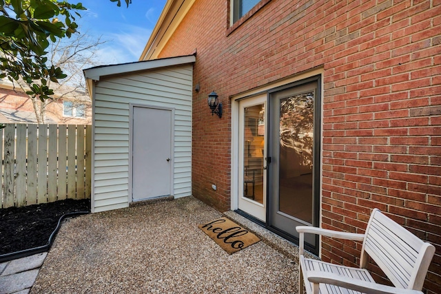 view of exterior entry with a patio area, fence, and brick siding