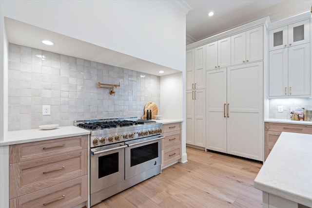 kitchen featuring light wood-style flooring, white cabinetry, light countertops, double oven range, and decorative backsplash