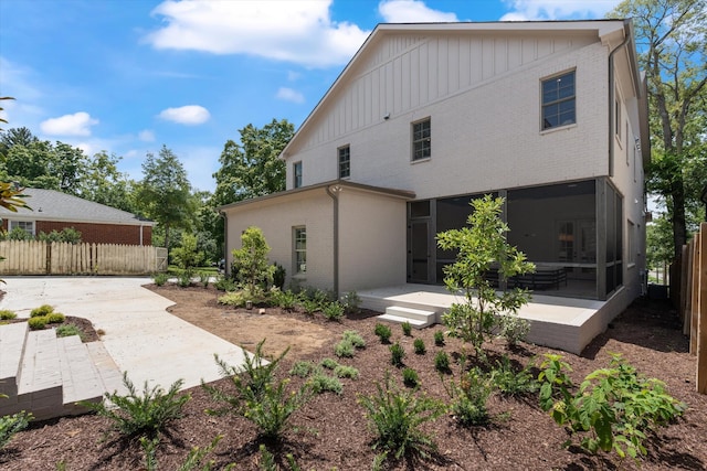 rear view of property featuring a patio, a sunroom, fence, board and batten siding, and brick siding