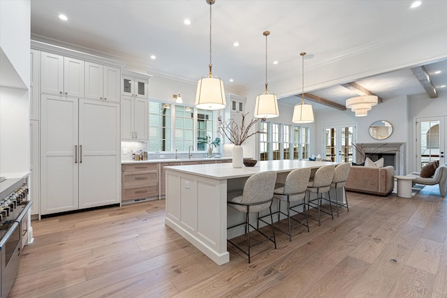 kitchen featuring a breakfast bar, a center island, light countertops, light wood-style floors, and glass insert cabinets