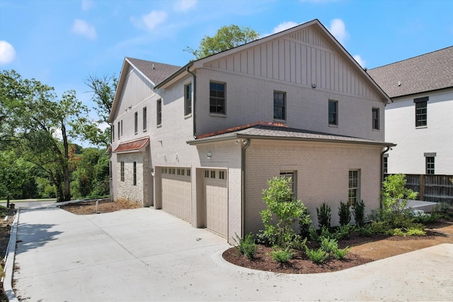 view of property exterior with an attached garage, driveway, board and batten siding, and brick siding