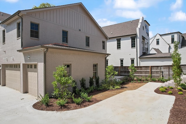 exterior space with brick siding, an attached garage, board and batten siding, fence, and driveway