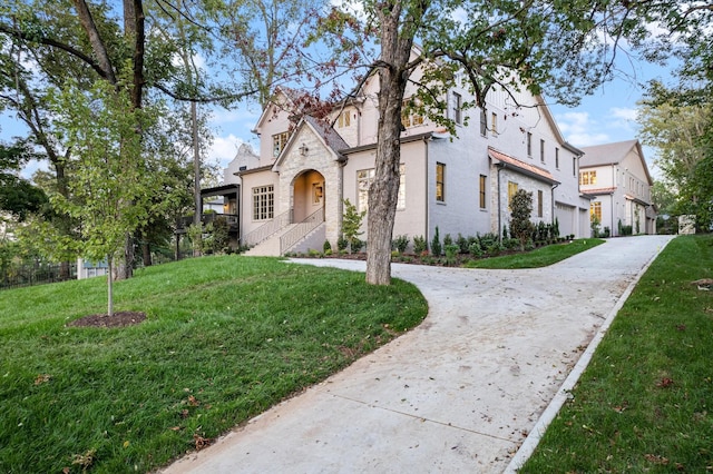 view of front of property with a front yard, stone siding, driveway, and stucco siding