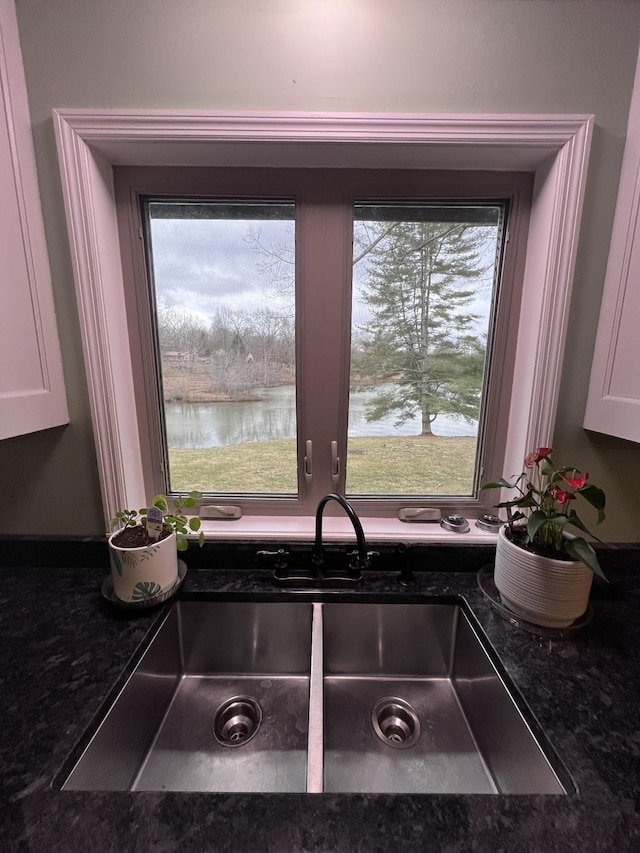 details featuring a water view, dark stone countertops, white cabinets, and a sink