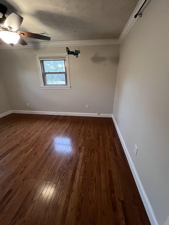 spare room with dark wood-type flooring, ornamental molding, baseboards, and a ceiling fan