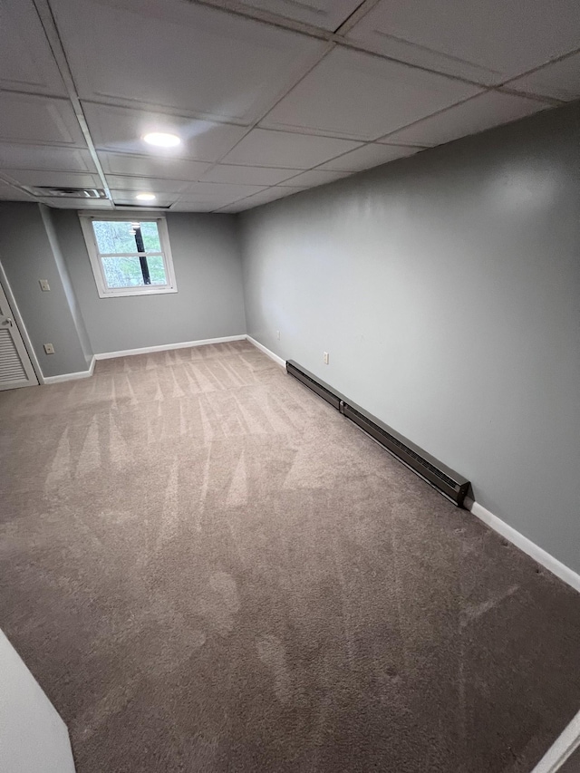 below grade area featuring a baseboard heating unit, a drop ceiling, carpet, and baseboards