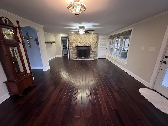 unfurnished living room with arched walkways, baseboards, dark wood-style floors, ceiling fan, and a stone fireplace