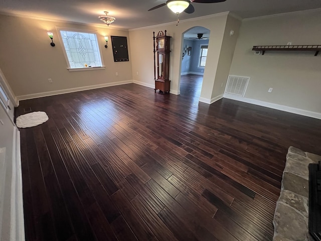 unfurnished living room featuring arched walkways, dark wood-type flooring, ornamental molding, and visible vents