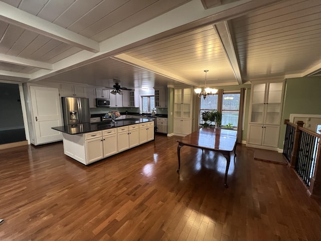 kitchen with dark wood finished floors, stainless steel appliances, dark countertops, white cabinets, and beamed ceiling