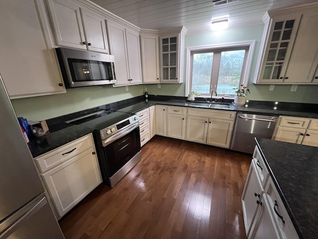 kitchen featuring dark wood-type flooring, a sink, appliances with stainless steel finishes, glass insert cabinets, and crown molding