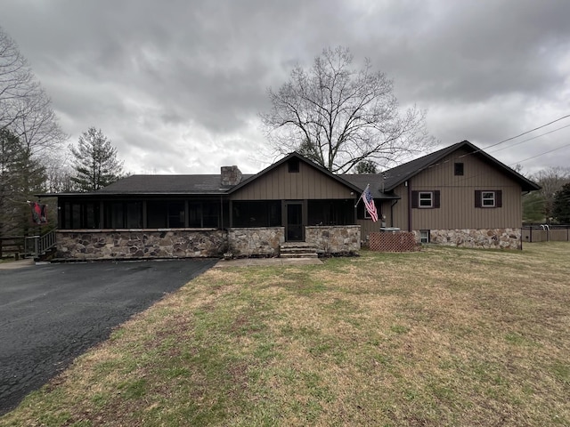 view of front of property with roof with shingles, a chimney, a sunroom, stone siding, and a front lawn