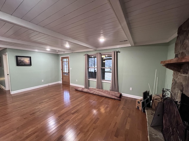 unfurnished living room featuring a stone fireplace, beamed ceiling, wood finished floors, and baseboards