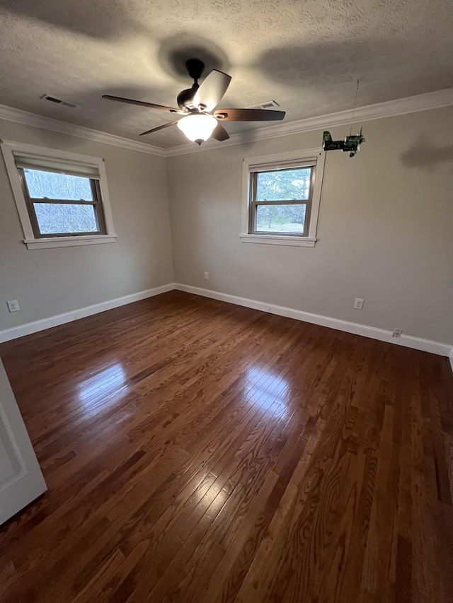 empty room with dark wood-style floors, a textured ceiling, baseboards, and crown molding