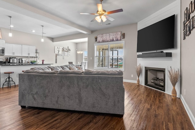 living room featuring beam ceiling, a fireplace, baseboards, and dark wood-type flooring