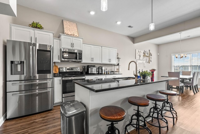 kitchen featuring dark wood-style floors, stainless steel appliances, dark countertops, visible vents, and an island with sink