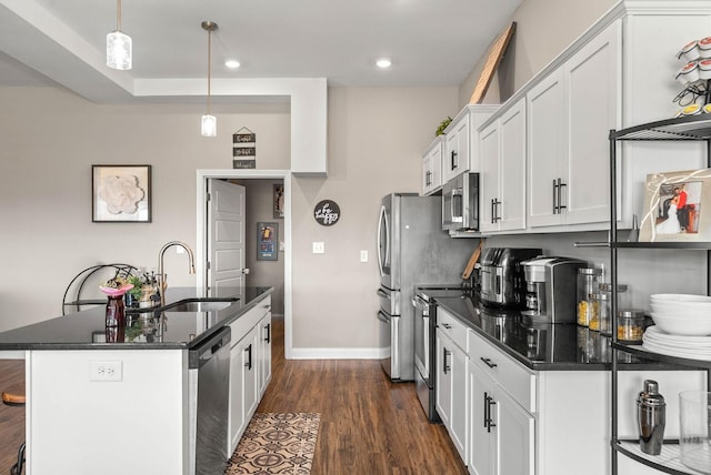 kitchen with white cabinets, appliances with stainless steel finishes, dark wood-style flooring, a kitchen island with sink, and a sink