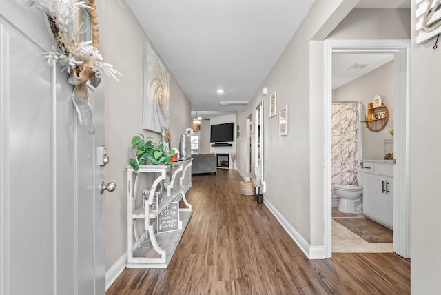 hall with wood finished floors, visible vents, and baseboards