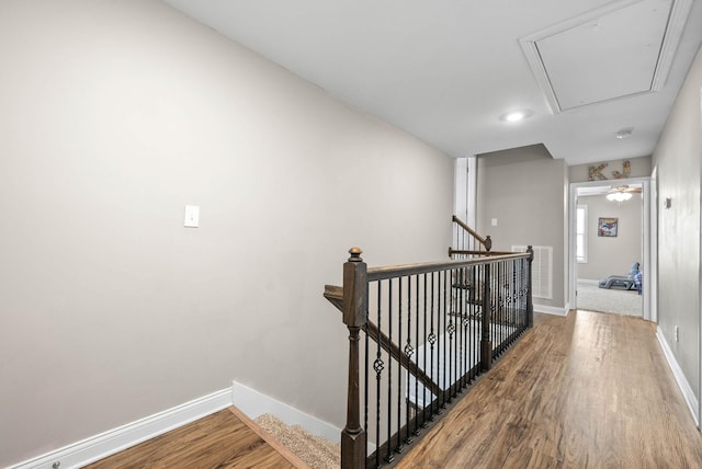 hallway with baseboards, wood finished floors, an upstairs landing, and attic access