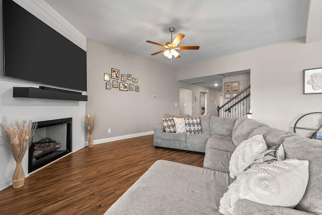 living area featuring baseboards, ceiling fan, wood finished floors, stairs, and a fireplace