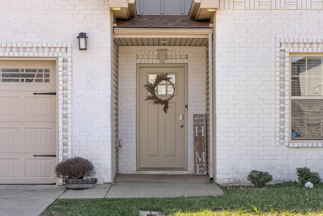 view of exterior entry featuring a shingled roof, brick siding, and a garage