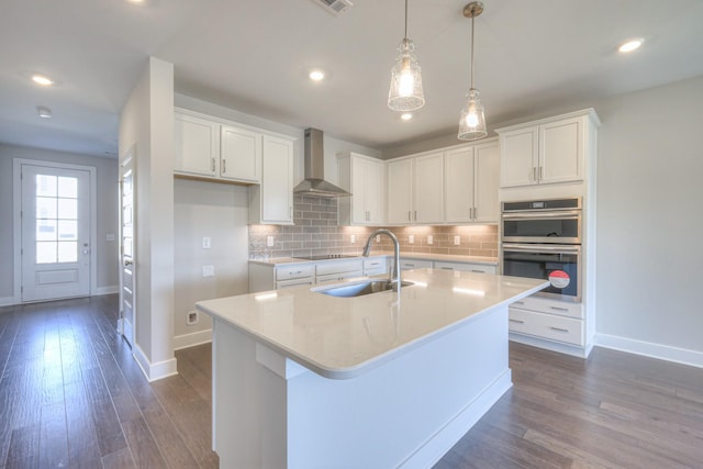 kitchen featuring double oven, black electric stovetop, dark wood-type flooring, a sink, and wall chimney exhaust hood