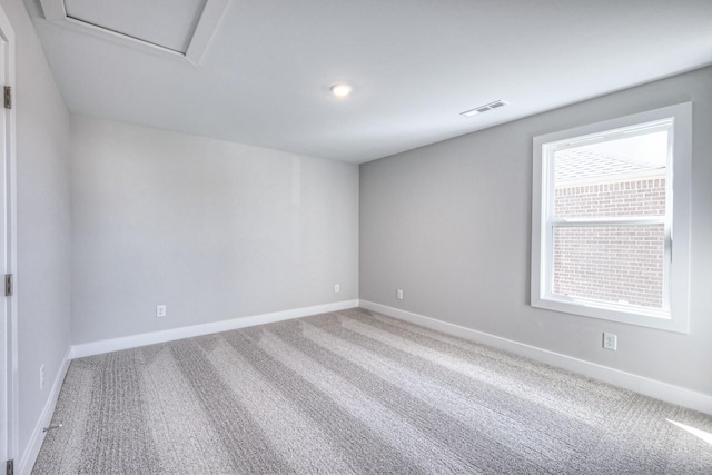 spare room featuring carpet floors, baseboards, visible vents, and attic access