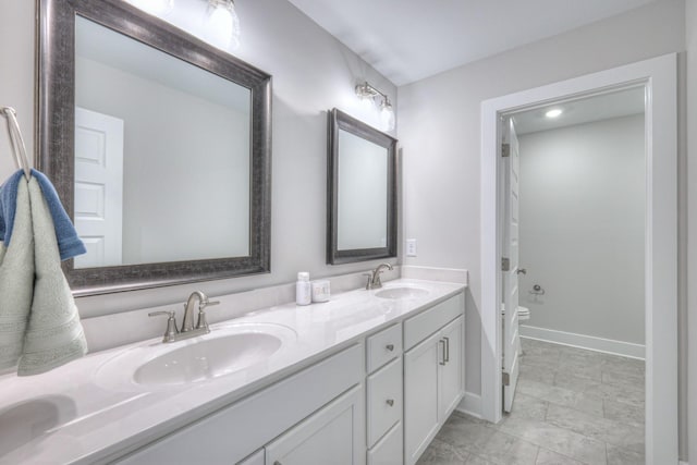 bathroom featuring baseboards, a sink, toilet, and double vanity