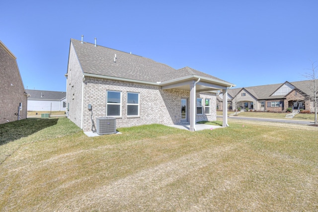 rear view of house featuring central air condition unit, roof with shingles, a lawn, and brick siding