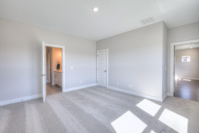 unfurnished bedroom featuring baseboards, ensuite bath, visible vents, and light colored carpet