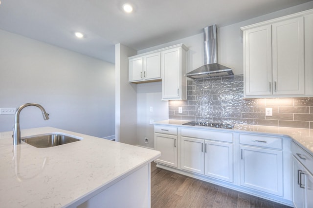 kitchen with wall chimney exhaust hood, black electric stovetop, a sink, and light stone counters