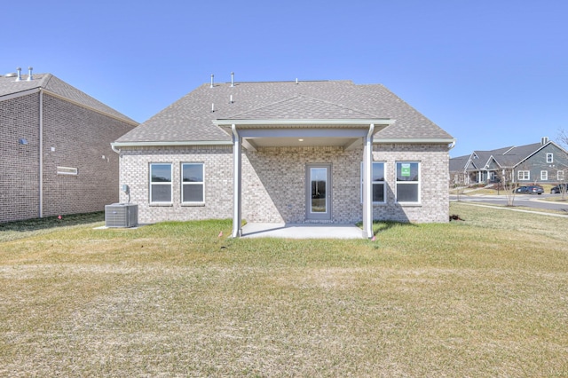 back of property with roof with shingles, brick siding, central air condition unit, a lawn, and a patio area