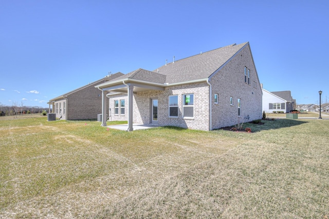 exterior space featuring central AC unit, a lawn, roof with shingles, a patio area, and brick siding